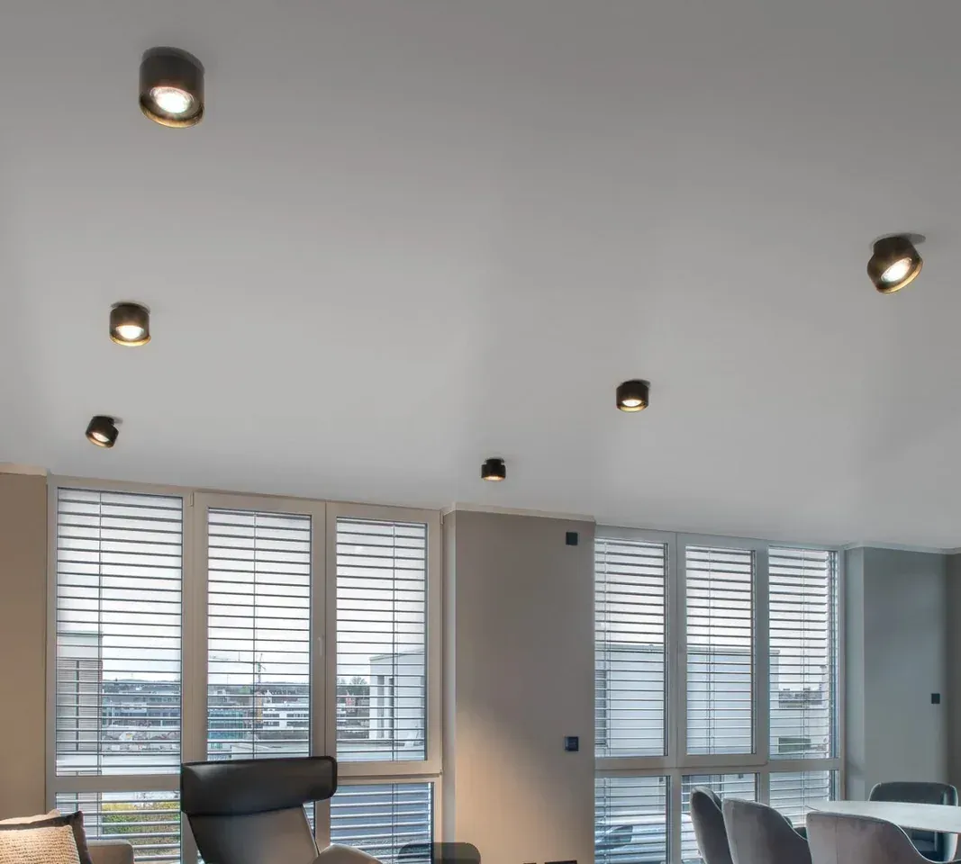 Wohnraum mit Fly Glas Aufbauspots in Rauchglas an der hellen Decke vor Fenstern mit Jalousien