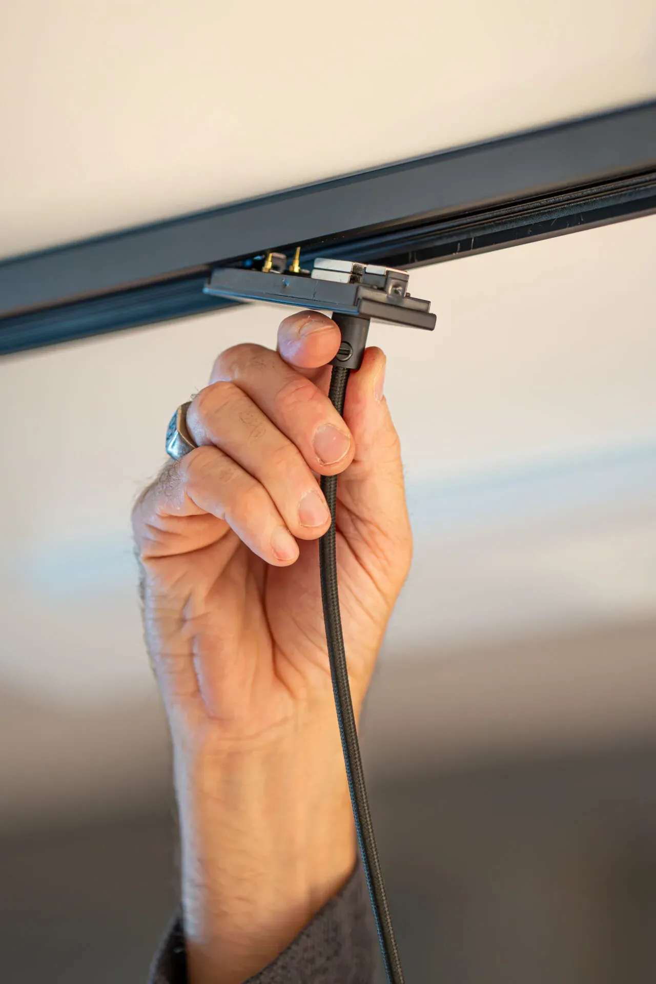 Hand hält den CLX-Adapter für Pendelleuchten mit Kabel an die schwarze TRIvario Schiene Hand hält den CLX-Adapter für Pendelleuchten mit Kabel an die schwarze TRIvario Schiene