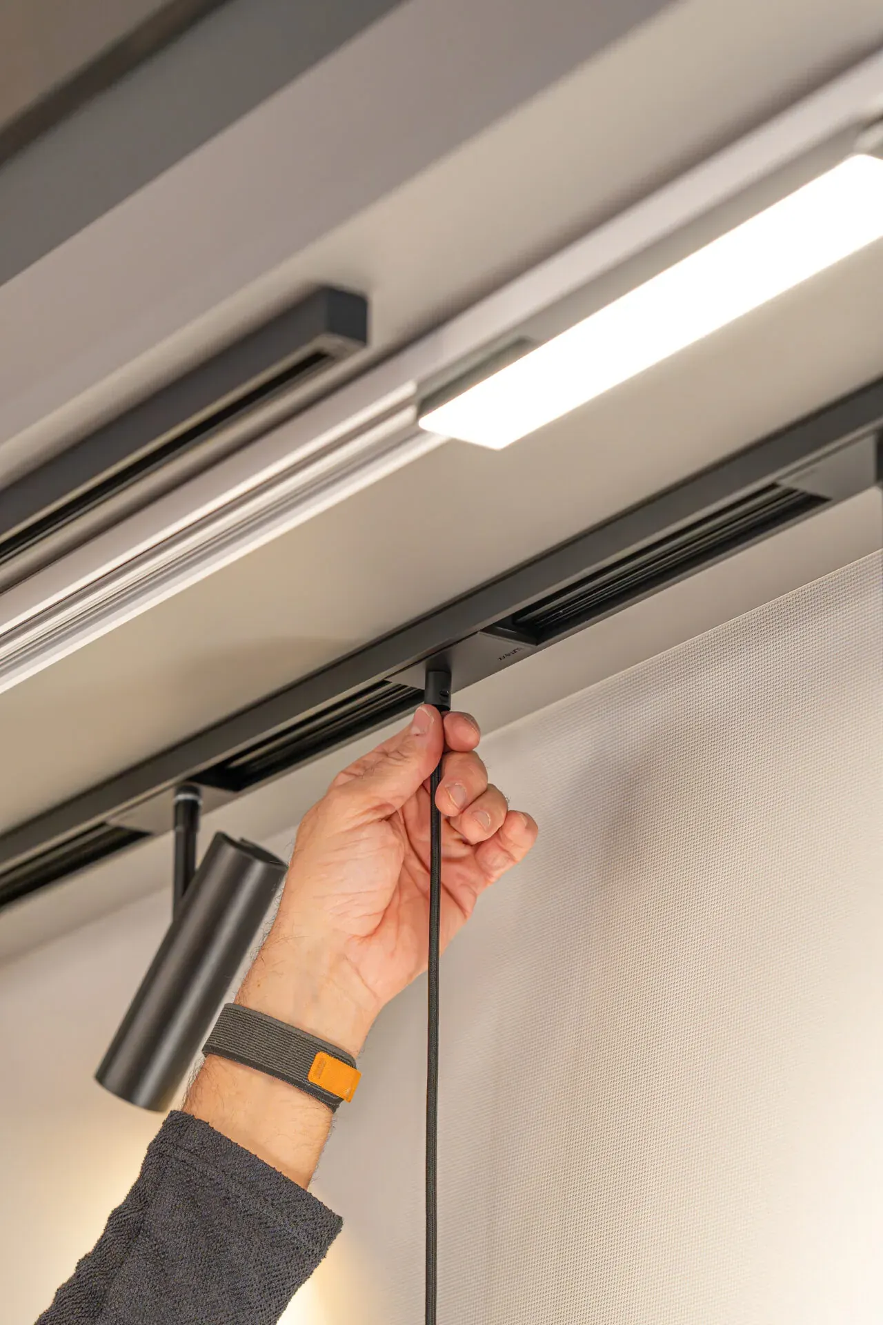 Hand setzt einen schwarzen Spot mit Kabel in die TRIvario Schiene, daneben ein Lichtband Hand setzt einen schwarzen Spot mit Kabel in die TRIvario Schiene, daneben ein Lichtband